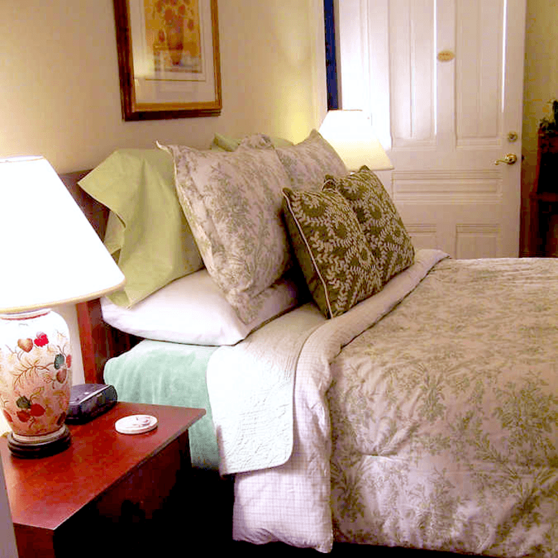 A cozy bedroom featuring a neatly made bed with green and floral patterned bedding and soft lighting.