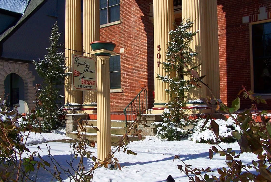 A cozy bed and breakfast with a sign, surrounded by snow-covered shrubs and columns.