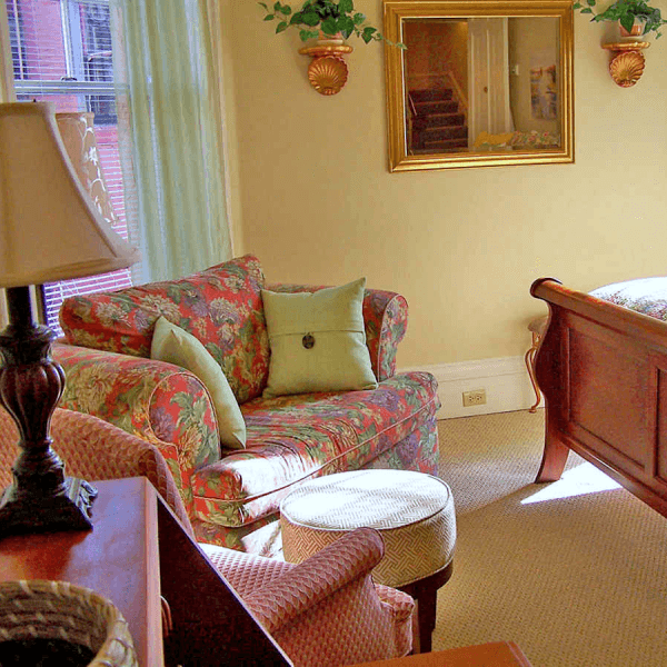 A cozy living room featuring a floral sofa, side table, and a mirror reflecting the space.