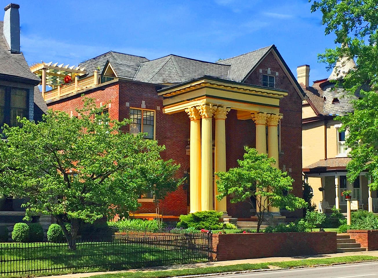 A large brick house with yellow columns and a landscaped yard under a clear blue sky.