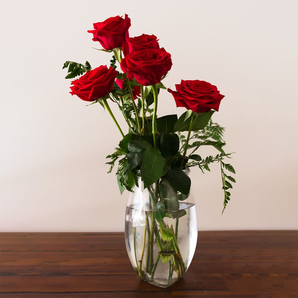 A vase of red roses and greenery on a wooden table.