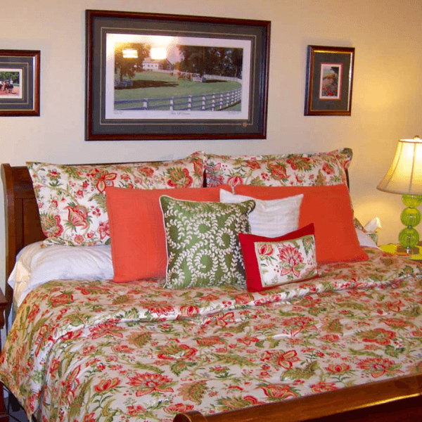A cozy bedroom featuring a floral-patterned bedspread and colorful decorative pillows, with framed artwork on the wall.
