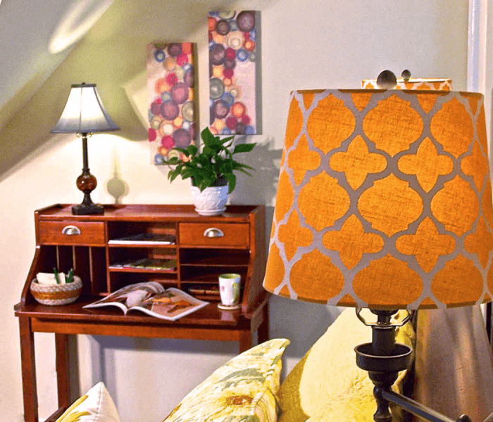 A cozy living space featuring a desk, decorative lamps, a plant, and artwork on the wall.