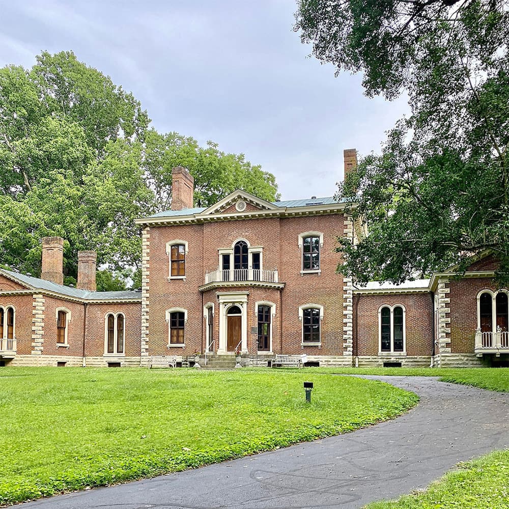 A historic brick mansion surrounded by lush greenery and a curved pathway.