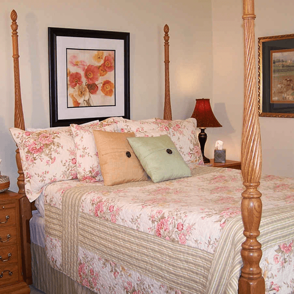 A cozy bedroom featuring a four-poster bed with floral bedding, decorative pillows, and artwork on the walls.