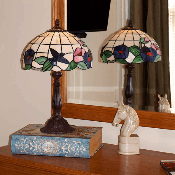 A vintage lamp with a stained glass shade and a ceramic horse figurine are placed on a decorative book in front of a mirror.
