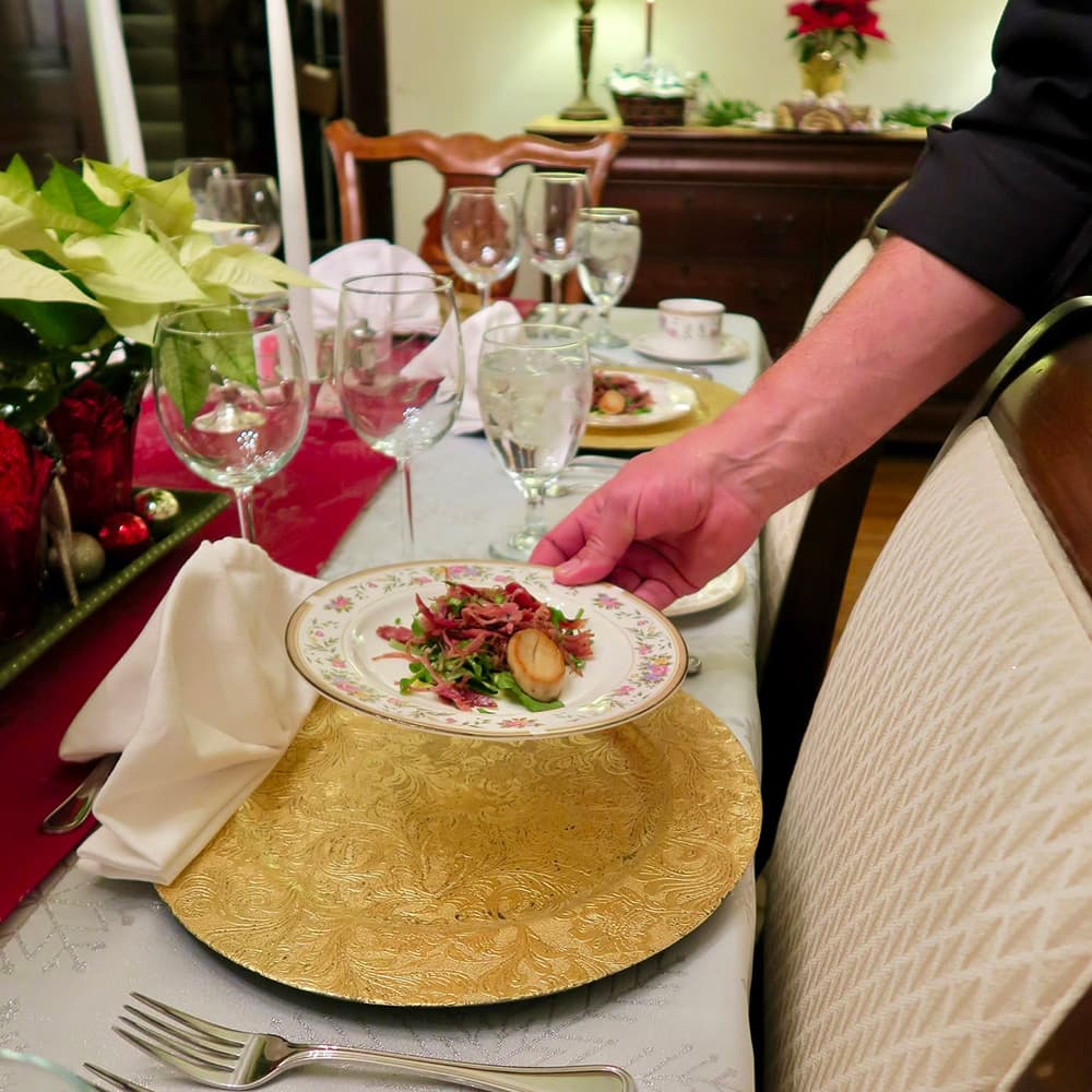 A person serves a plate of salad at an elegantly set dining table.