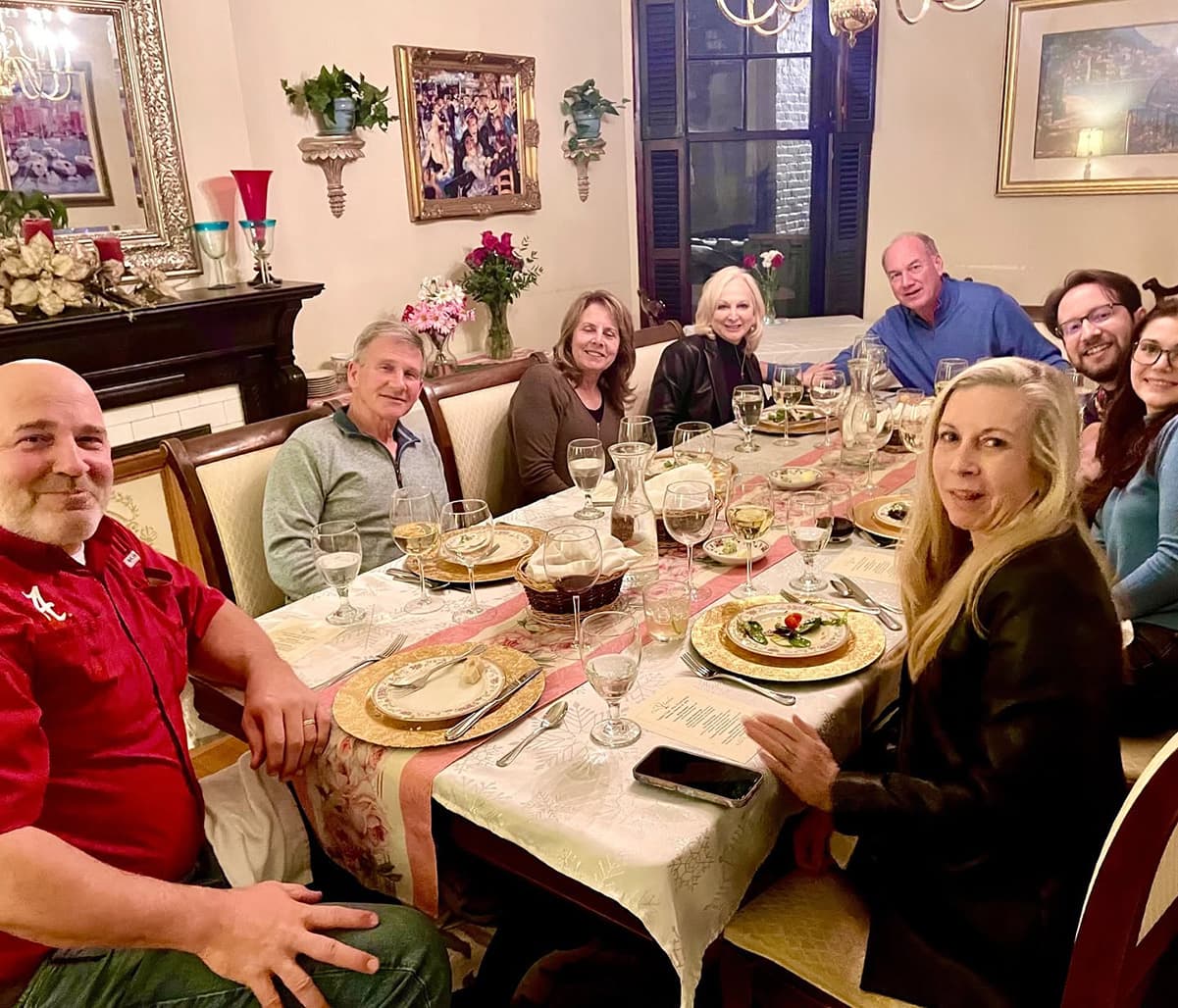 A group of eight people smiles around a festive dining table set with plates and glasses.