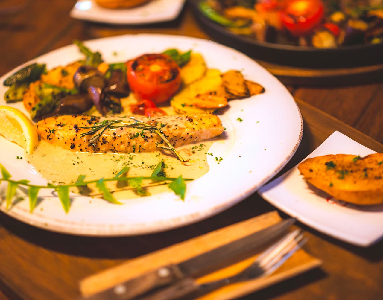 A plate of grilled salmon accompanied by roasted potatoes, vegetables, and a slice of lemon.
