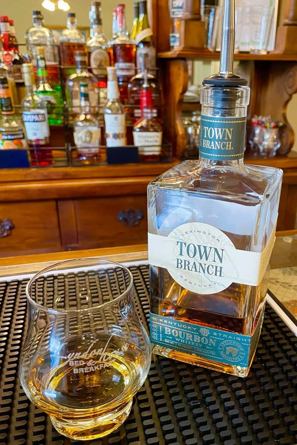 A bottle of Town Branch bourbon next to a glass with a pour of whiskey on a bar countertop.