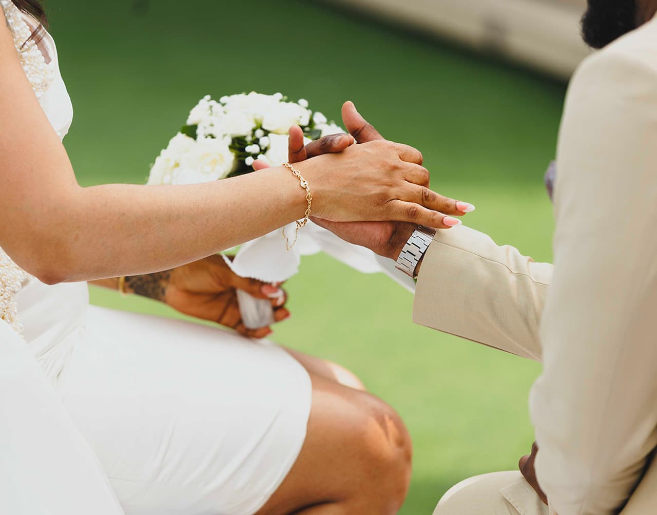 A close-up of two hands holding each other, with a bouquet of white flowers in the background.