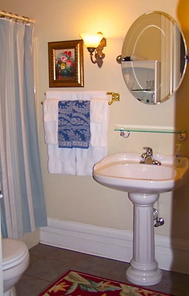 A small, well-decorated bathroom featuring a pedestal sink, mirror, artwork, and towels.