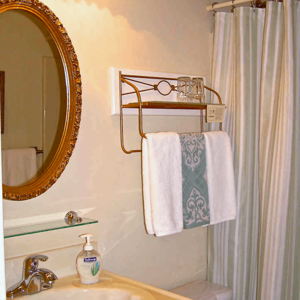 A bathroom scene featuring a round mirror, a towel rack with a towel and glasses, and soap on a sink.