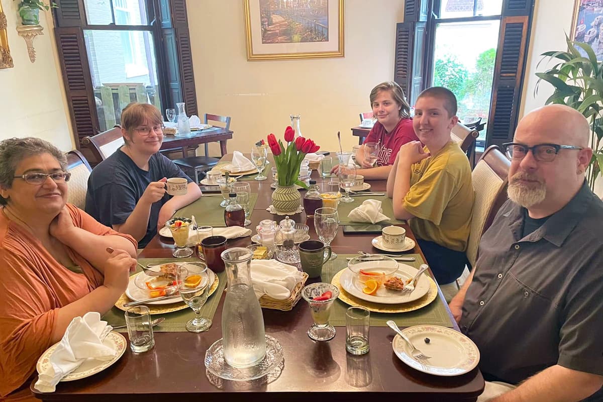 A group of five people enjoying a meal at a beautifully set table with flowers and various dishes.