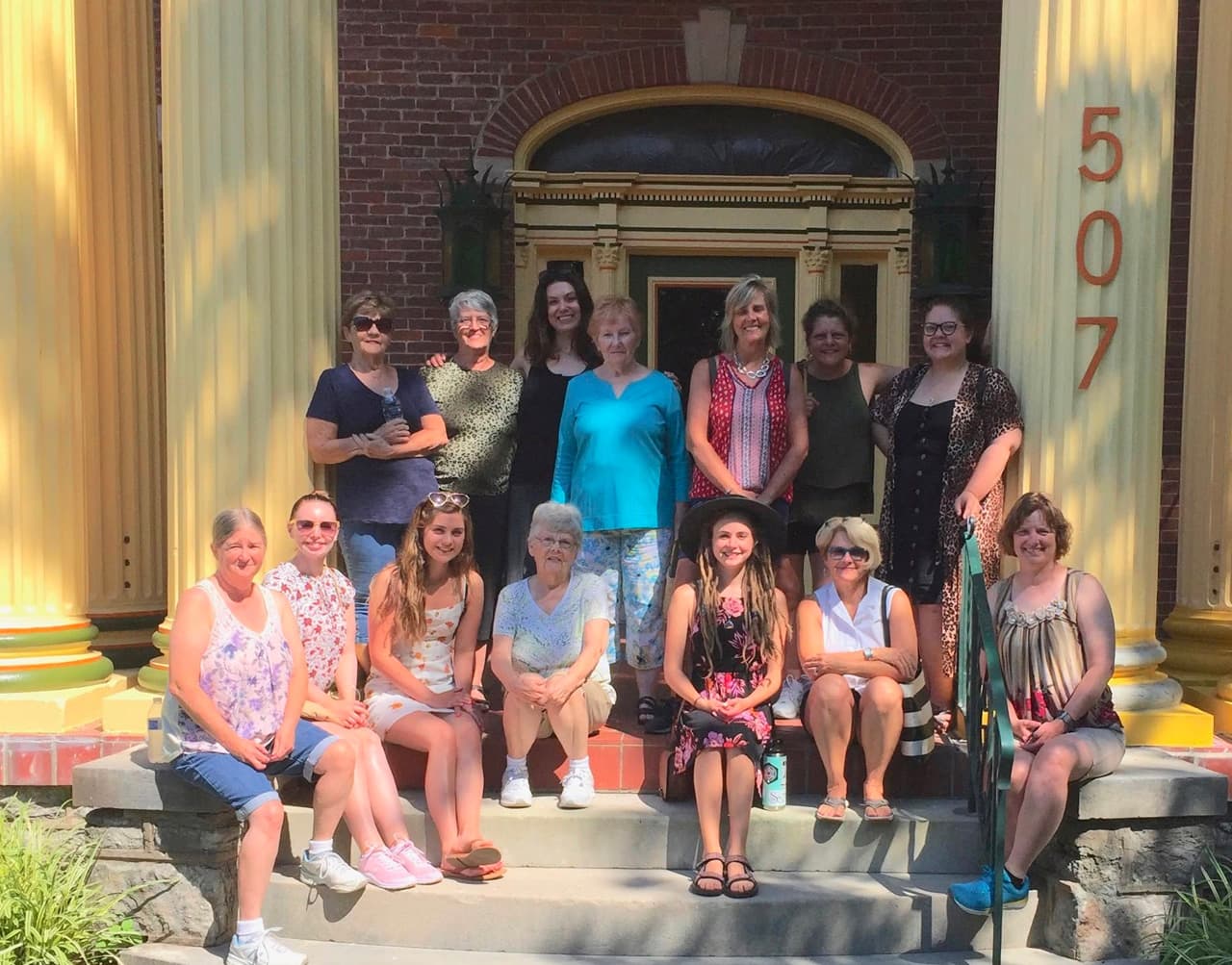 A group of women posed together on the steps of a building with yellow columns.