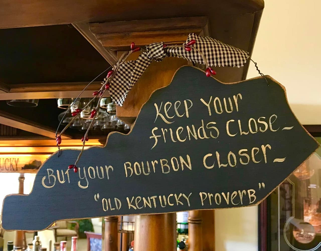 A wooden sign in the shape of Kentucky reads, "Keep your friends close - but your bourbon closer - 'Old Kentucky Proverb'."
