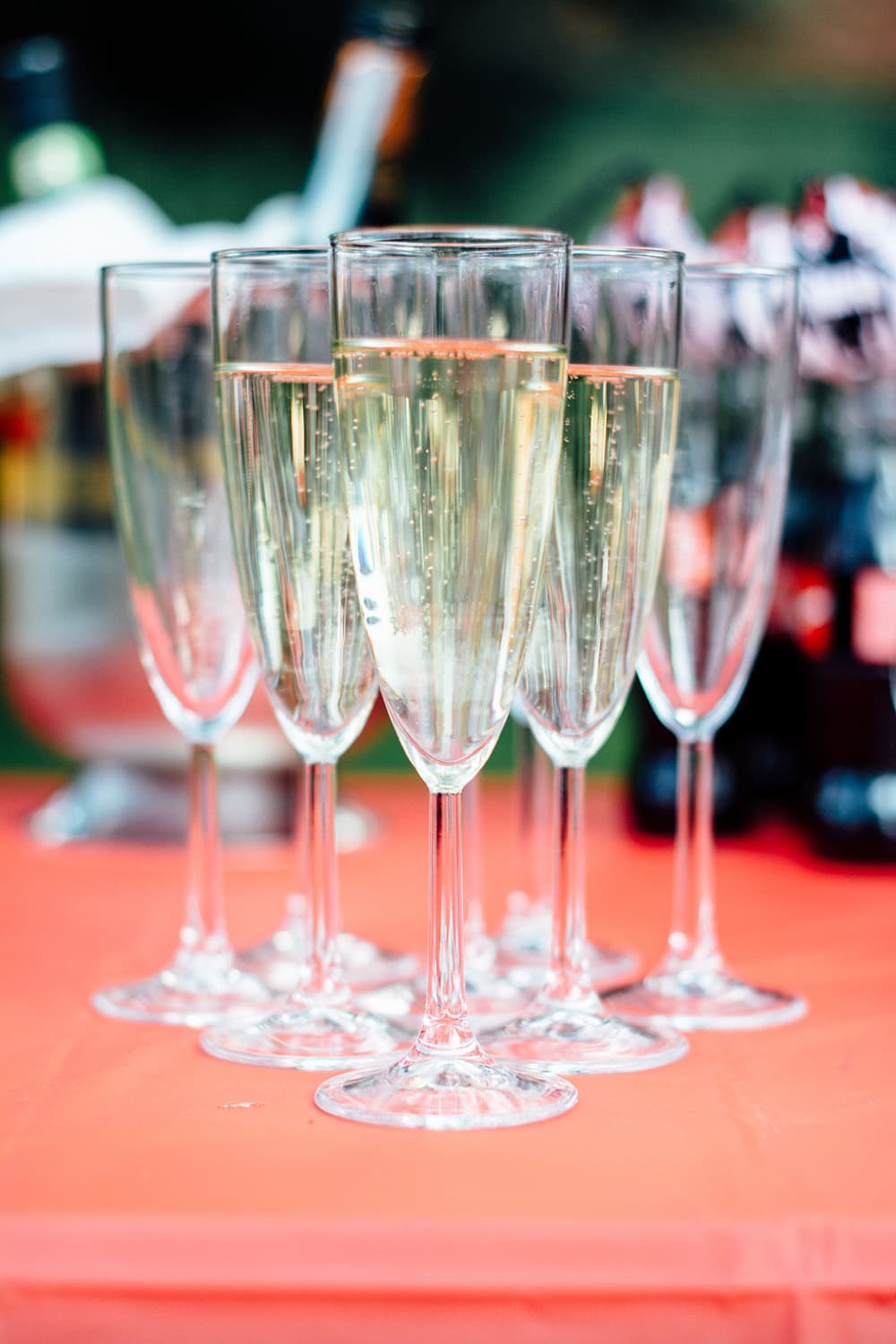 A row of champagne flutes filled with sparkling drink on an orange tablecloth.