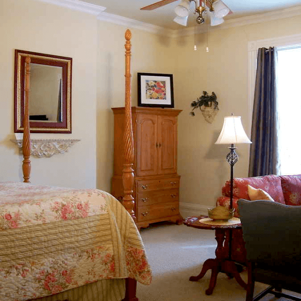 A cozy bedroom featuring a four-poster bed, an armoire, a lamp, and a floral sofa.
