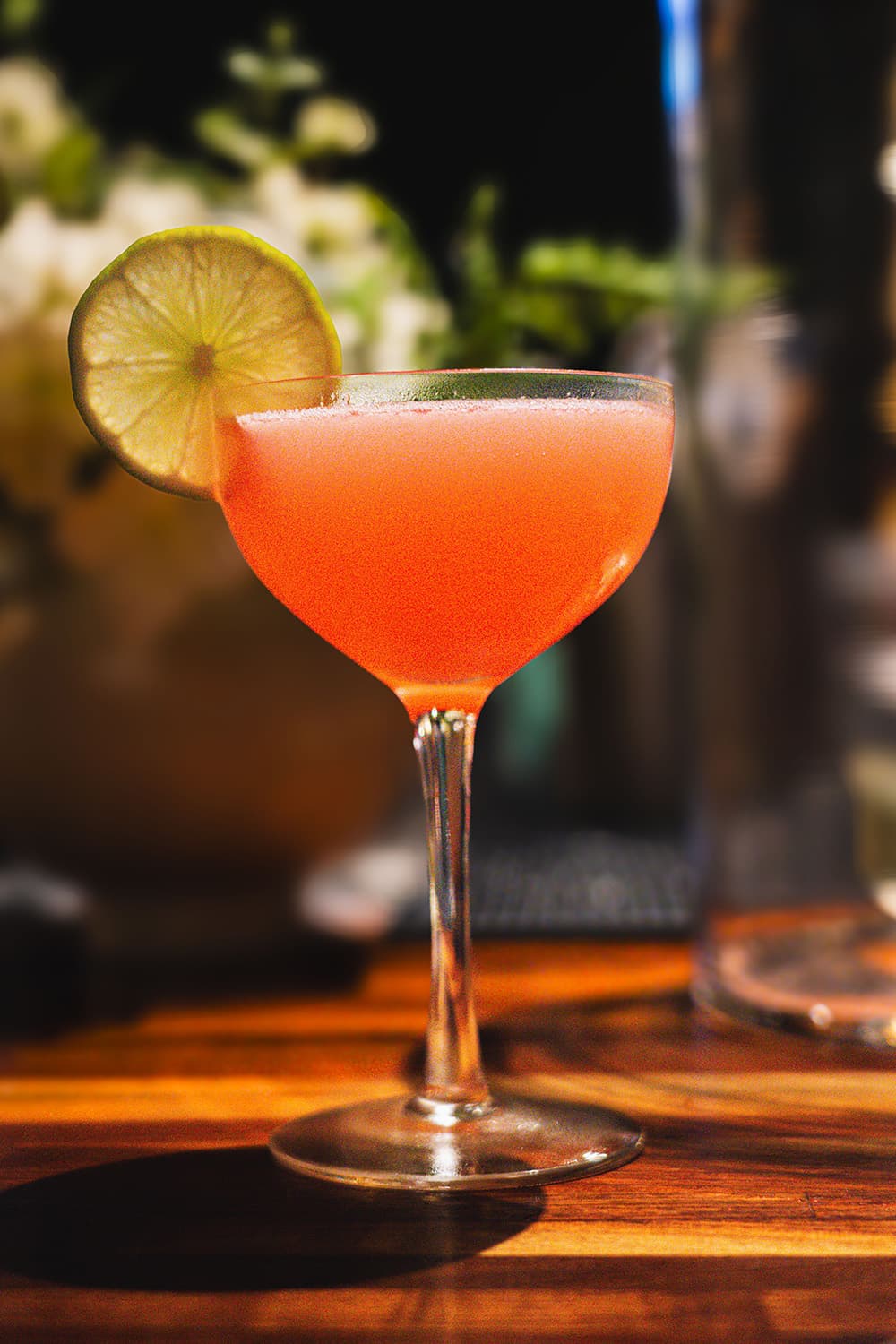 A bright pink cocktail garnished with a lime slice, set against a blurred background.