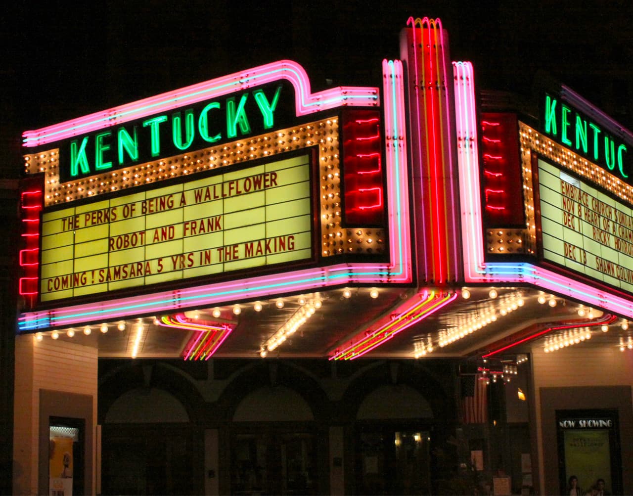 Brightly lit theater marquee for "Kentucky" displaying movie titles and showtimes.