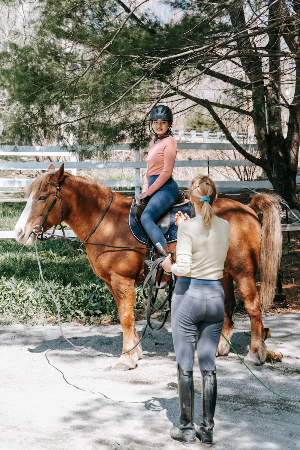 A woman sits on a horse while another woman stands nearby holding a lead rope.