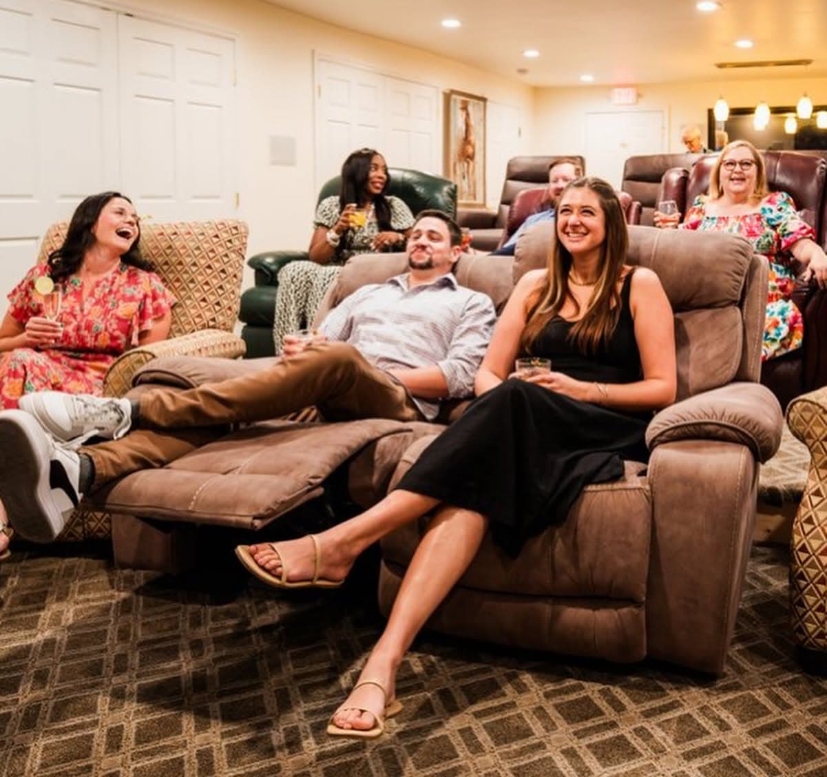 A group of people relaxes in recliners, enjoying drinks and laughter in a cozy lounge setting.