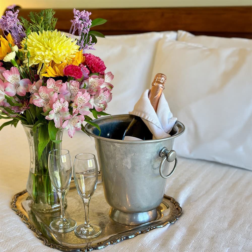 A bouquet of colorful flowers beside a silver ice bucket holding a champagne bottle and two fluted glasses on a tray.