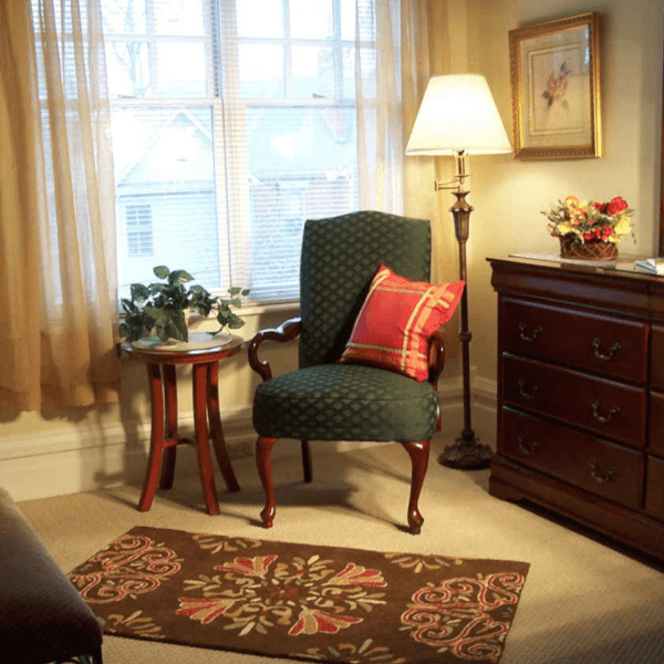 Cozy corner featuring a green upholstered chair, a side table with a plant, a lamp, and a wooden dresser.