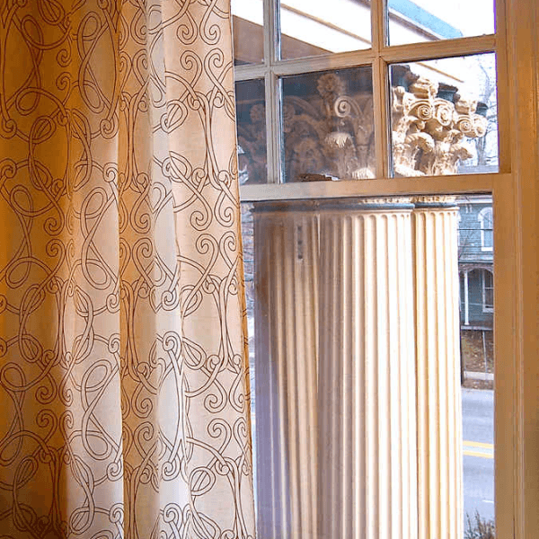 A window with decorative curtains revealing a view of classic architectural columns.