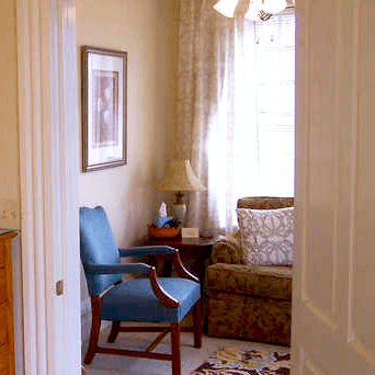 A cozy living room corner featuring an armchair, a patterned sofa, and a lamp by the window.