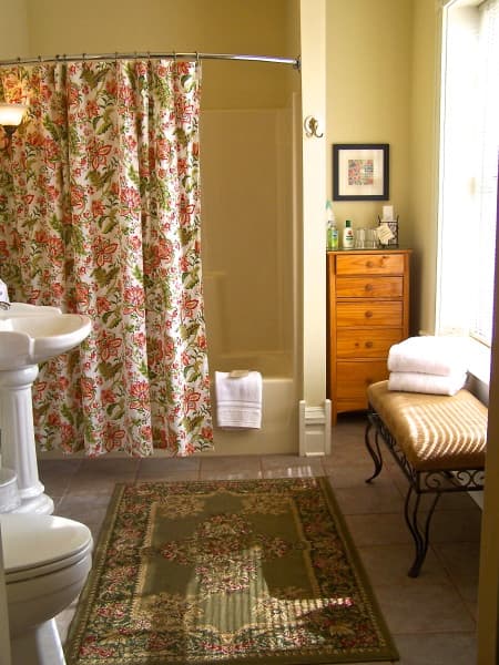 A cozy bathroom featuring a floral shower curtain, a sink, a wooden dresser, and neatly arranged towels.