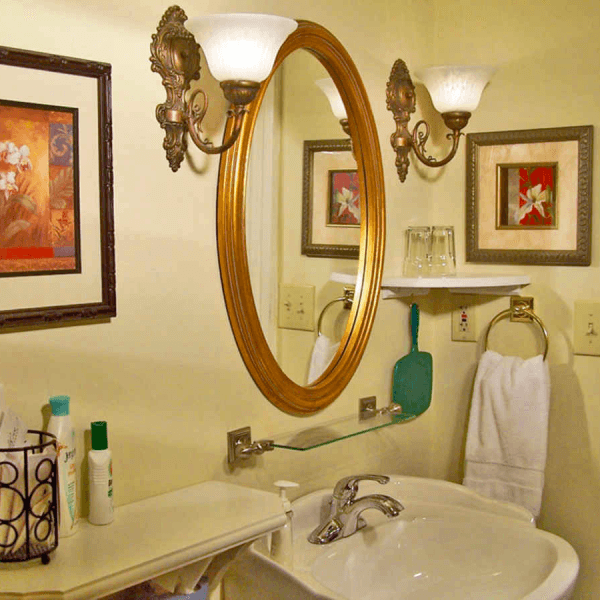 A vintage bathroom featuring an ornate round mirror, decorative sconces, and neatly arranged toiletries.