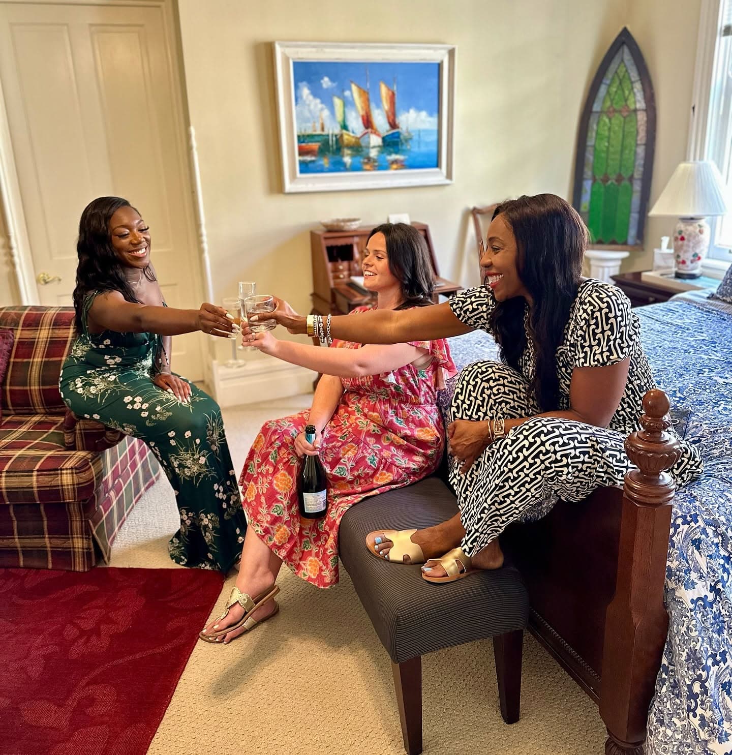 Three women toast with drinks in a cozy room filled with cheerful decor.