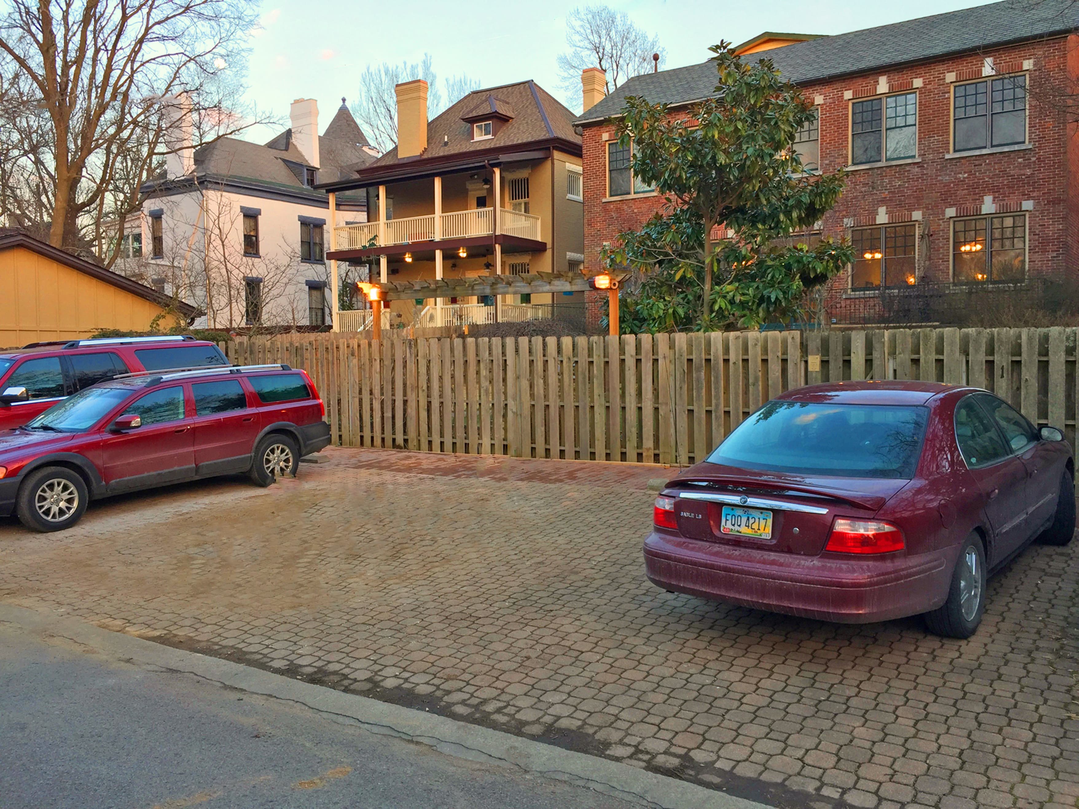 A row of parked cars in a cobblestone lot with historical buildings in the background.